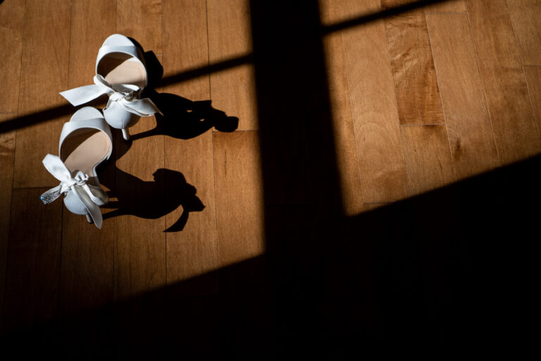 bride's high heels with ribbons on the ankle straps photographed on a wood floor in the sunlight coming through a window