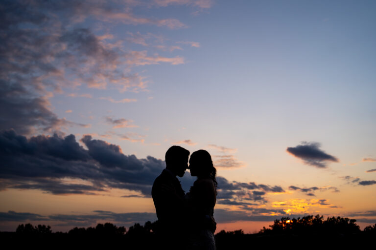 silhouette of bride and groom holding each other face to face about to kiss with a dramatic sunset in the background
