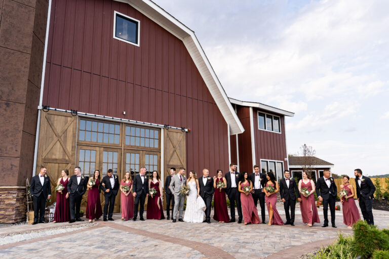 bride and group surrounded by large bridal party of 20 as entire group stands in front of the Barn at Villa Venezia in Middletown, NY on a bright summer day