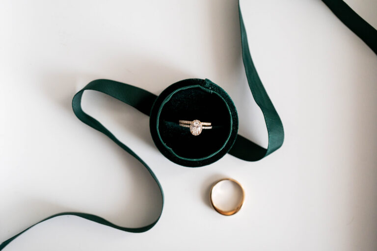 double banded wedding ring placed inside circular green velvet ring box with green ribbon and groom's ring next to it