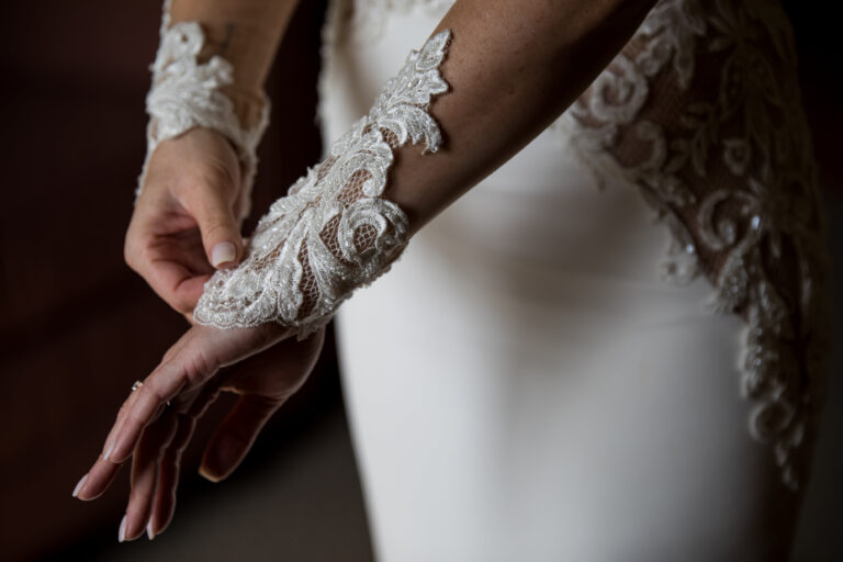 dramatic closeup of bride with manicured nails adjusting embroidered lace sleeves while wearing ornate lace wedding gown