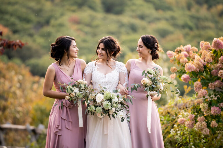 A bride with her two bridesmaids holding their bouquets and looking at each other at the top of Lambs Hill in Beacon NY