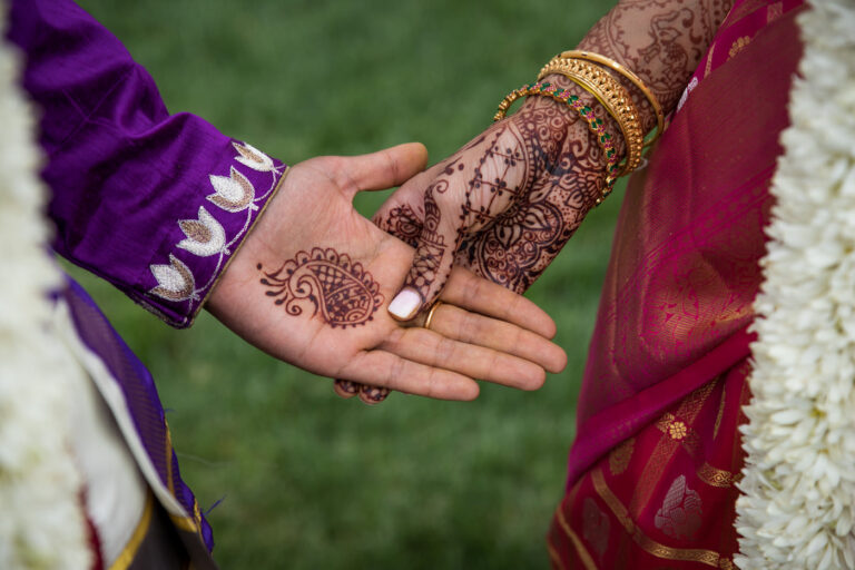 closeup of bride and groom hands covered in henna tattoo with bright traditional Indian marriage attire and jewelry
